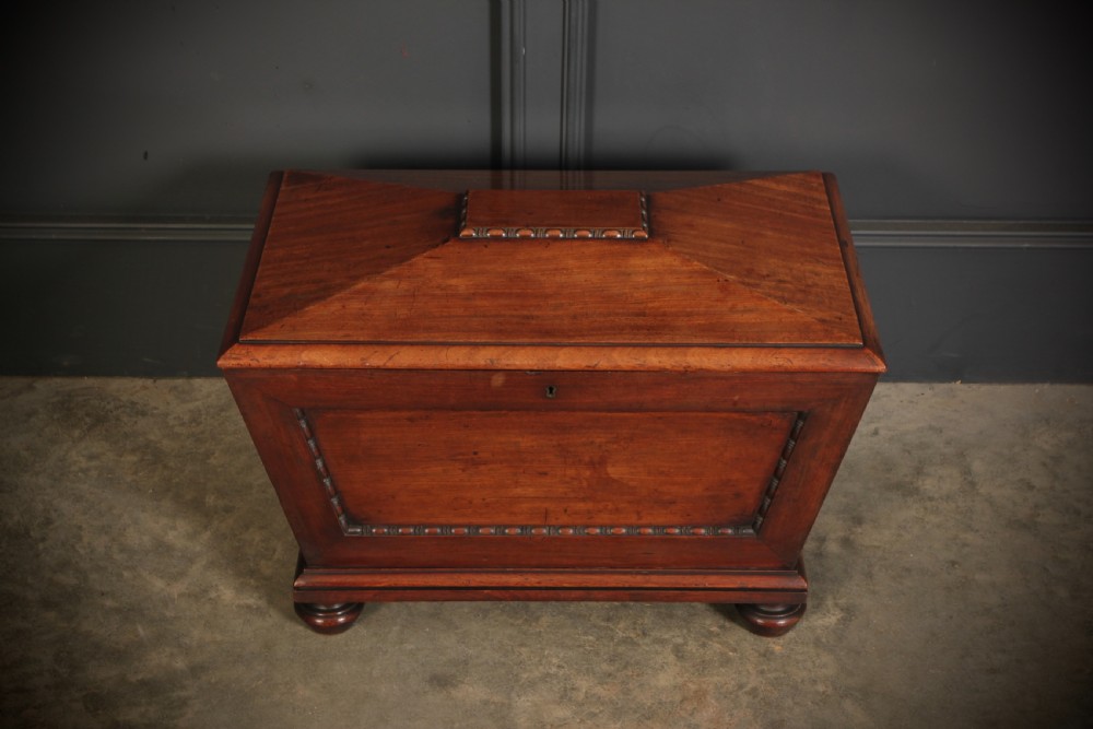 A Regency period mahogany sarcophagus cellarette featuring tapered sides, beaded moulding, and compressed turned feet. View V