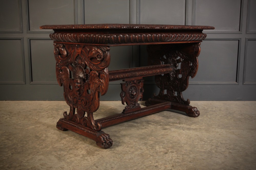 A dark walnut centre table featuring ornate carved trestle supports, carved human and animal masks, a gadrooned apron, and lion paw feet.