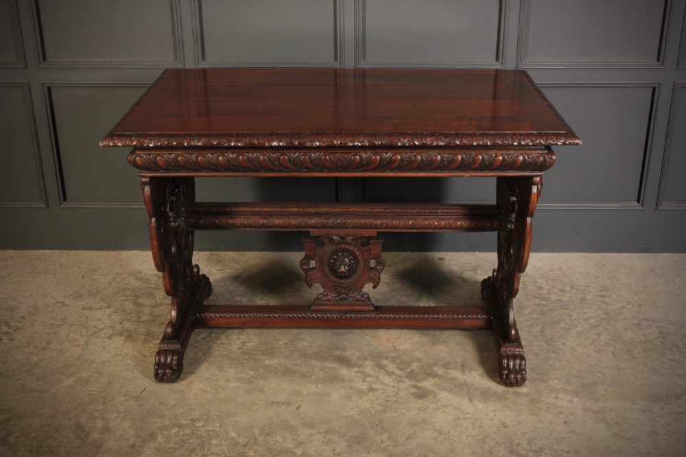 A dark walnut centre table featuring ornate carved trestle supports, carved human and animal masks, a gadrooned apron, and lion paw feet. View V