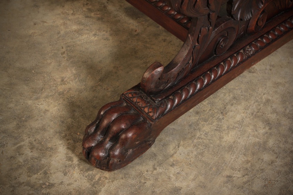 A dark walnut centre table featuring ornate carved trestle supports, carved human and animal masks, a gadrooned apron, and lion paw feet. View X