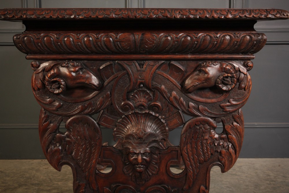 A dark walnut centre table featuring ornate carved trestle supports, carved human and animal masks, a gadrooned apron, and lion paw feet. View XII