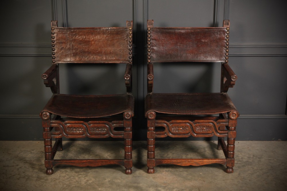 A pair of carved dark oak armchairs featuring stretched dark brown leather seats and backs fixed with brass metal studs. View II
