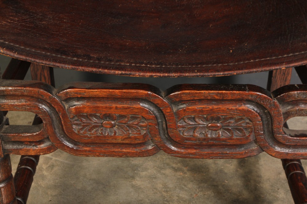 A pair of carved dark oak armchairs featuring stretched dark brown leather seats and backs fixed with brass metal studs. View VI