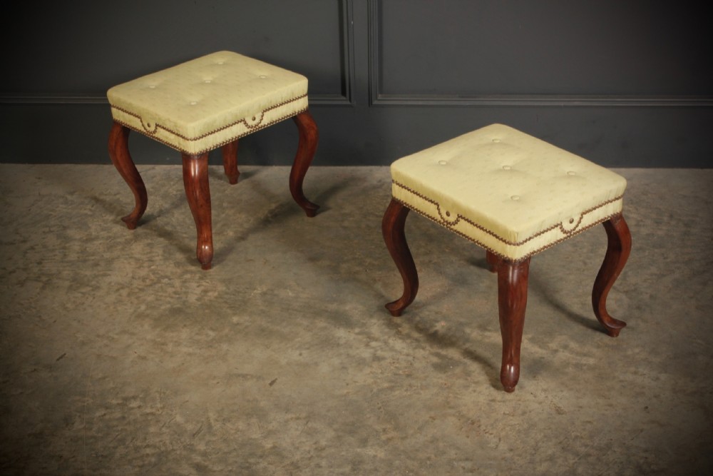 A pair of early Victorian footstools featuring dark mahogany cabriole legs and cream silk buttoned upholstered tops with brass stud detail.