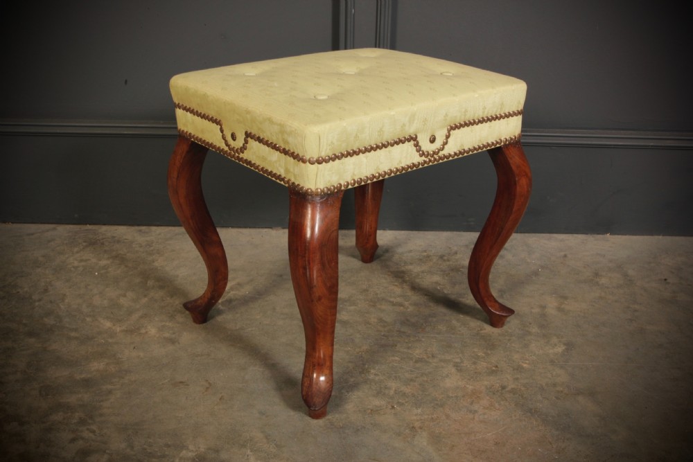 A pair of early Victorian footstools featuring dark mahogany cabriole legs and cream silk buttoned upholstered tops with brass stud detail. View V