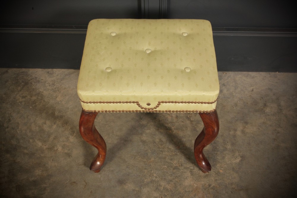 A pair of early Victorian footstools featuring dark mahogany cabriole legs and cream silk buttoned upholstered tops with brass stud detail. View VI
