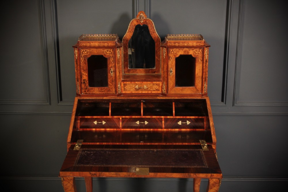 A Victorian burr walnut bonheur du jour writing desk featuring intricate floral marquetry, cabriole legs, brass mounts, and a raised superstructure with small glass cabinets. View III