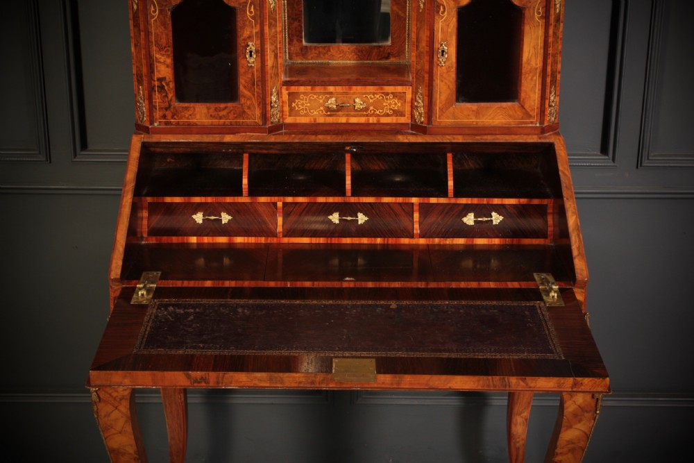 A Victorian burr walnut bonheur du jour writing desk featuring intricate floral marquetry, cabriole legs, brass mounts, and a raised superstructure with small glass cabinets. View IV
