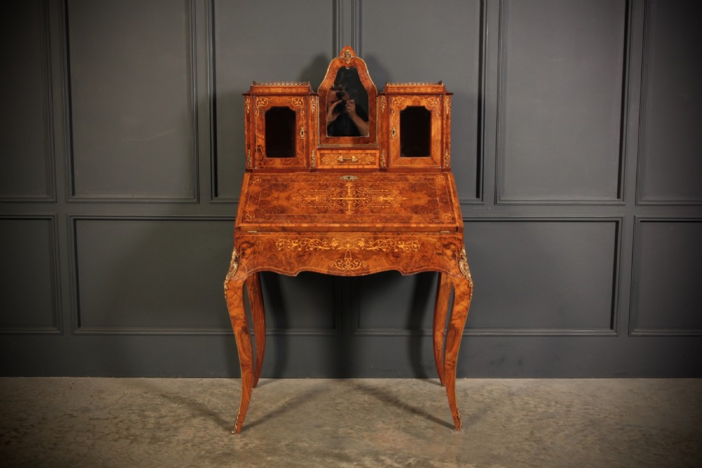A Victorian burr walnut bonheur du jour writing desk featuring intricate floral marquetry, cabriole legs, brass mounts, and a raised superstructure with small glass cabinets. View VI