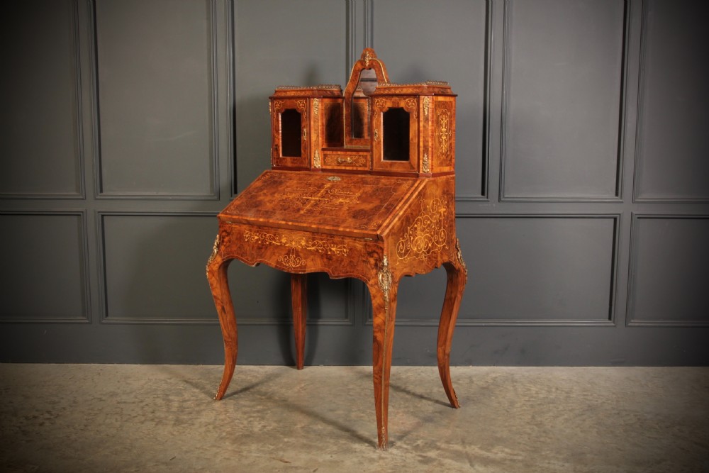 A Victorian burr walnut bonheur du jour writing desk featuring intricate floral marquetry, cabriole legs, brass mounts, and a raised superstructure with small glass cabinets. View X