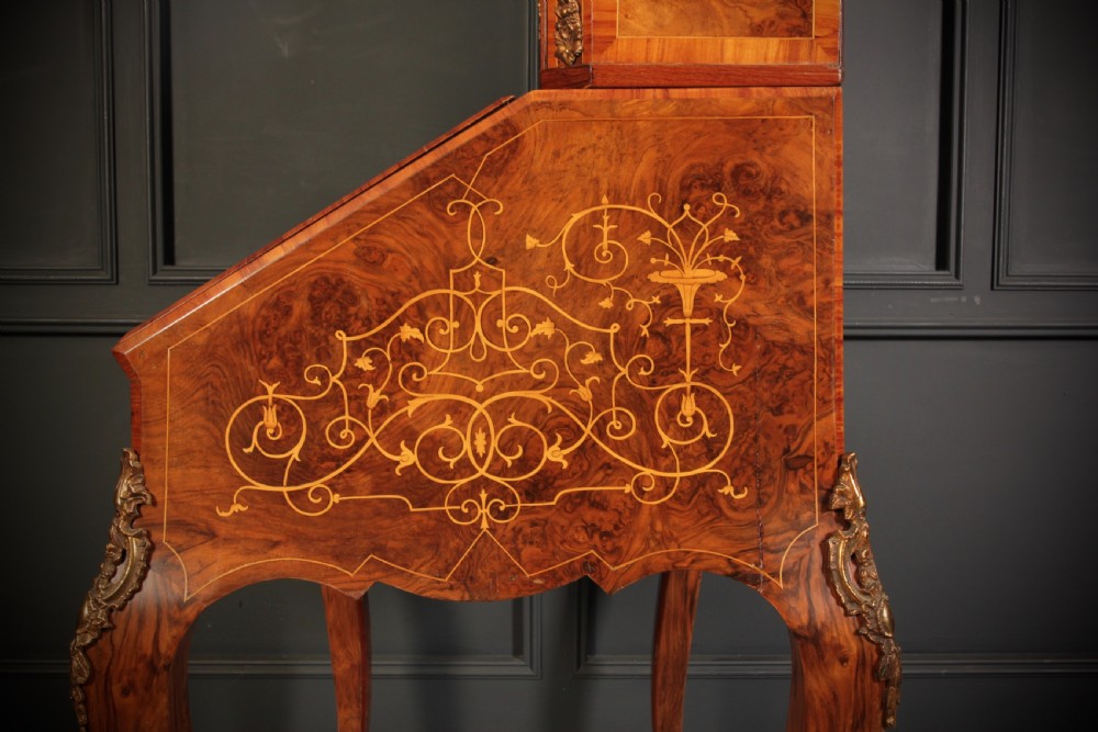 A Victorian burr walnut bonheur du jour writing desk featuring intricate floral marquetry, cabriole legs, brass mounts, and a raised superstructure with small glass cabinets. View XVI
