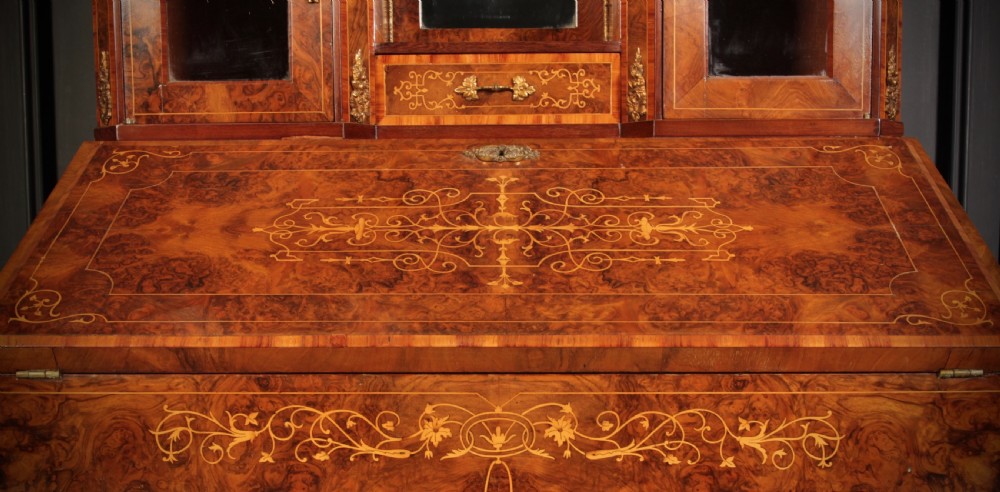 A Victorian burr walnut bonheur du jour writing desk featuring intricate floral marquetry, cabriole legs, brass mounts, and a raised superstructure with small glass cabinets. View XIX