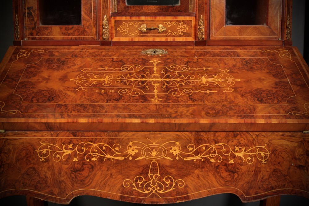 A Victorian burr walnut bonheur du jour writing desk featuring intricate floral marquetry, cabriole legs, brass mounts, and a raised superstructure with small glass cabinets. View XX