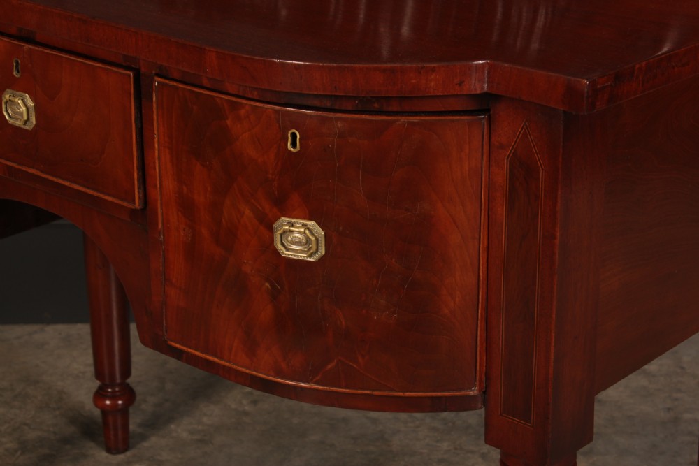 A William IV flame mahogany bow-front sideboard featuring a carved scroll backboard, flame veneer drawer fronts, brass keyhole escutcheons, and spiral-turned front legs. View VIII