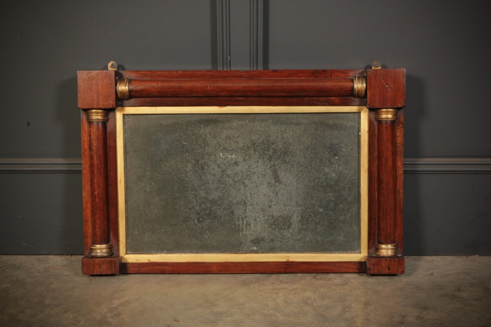 A rectangular antique rosewood overmantel mirror featuring classical side columns with gilt capitals and foxed mirror glass.