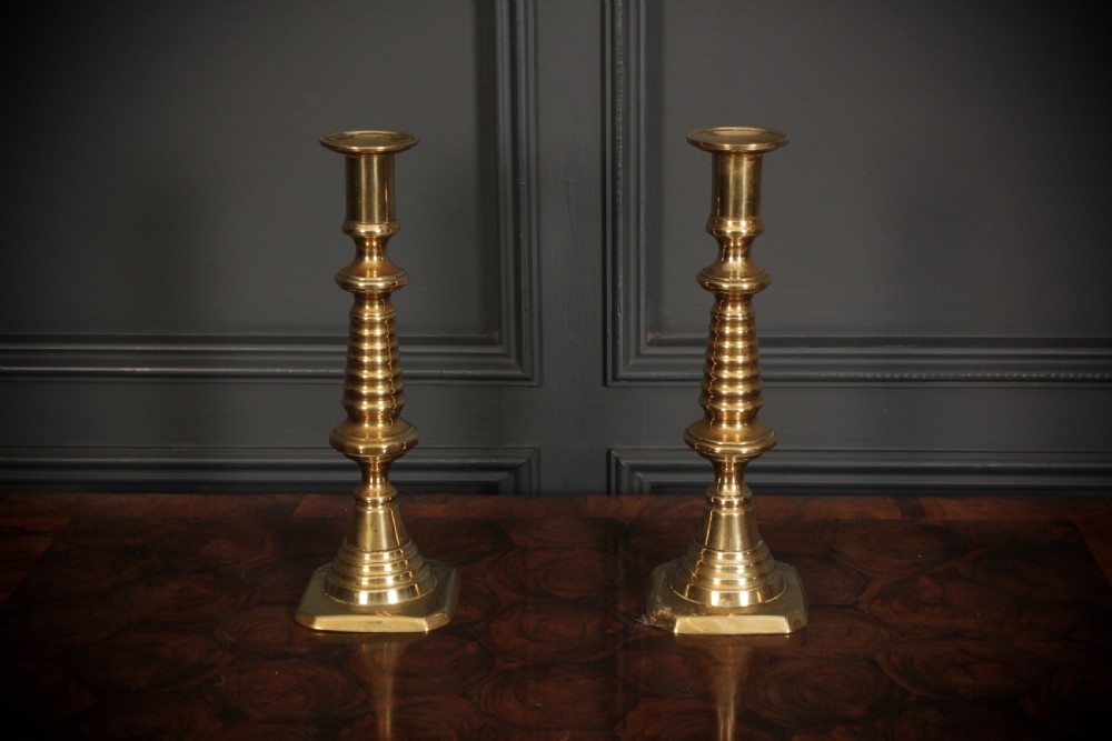 A pair of tall Victorian brass candlesticks featuring turned stems and stepped square bases. View II
