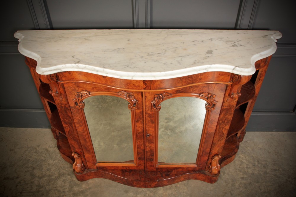 A Victorian burr walnut side cabinet featuring a white marble top, curved side shelves, and mirrored doors flanked by carved corbels. View VI