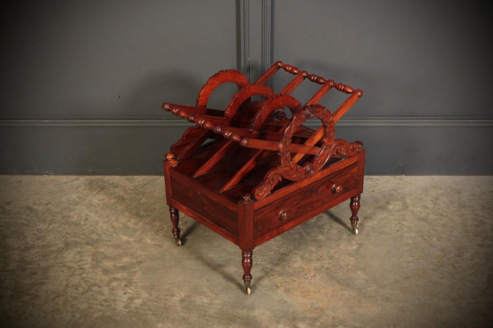 A William IV dark rosewood Canterbury magazine rack featuring four open compartments with carved decorative divisions above a single base drawer on turned legs with brass castors. View III