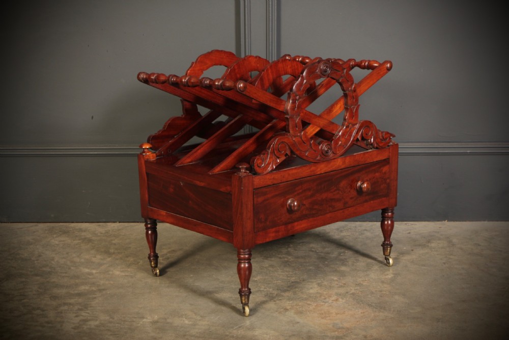 A William IV dark rosewood Canterbury magazine rack featuring four open compartments with carved decorative divisions above a single base drawer on turned legs with brass castors.