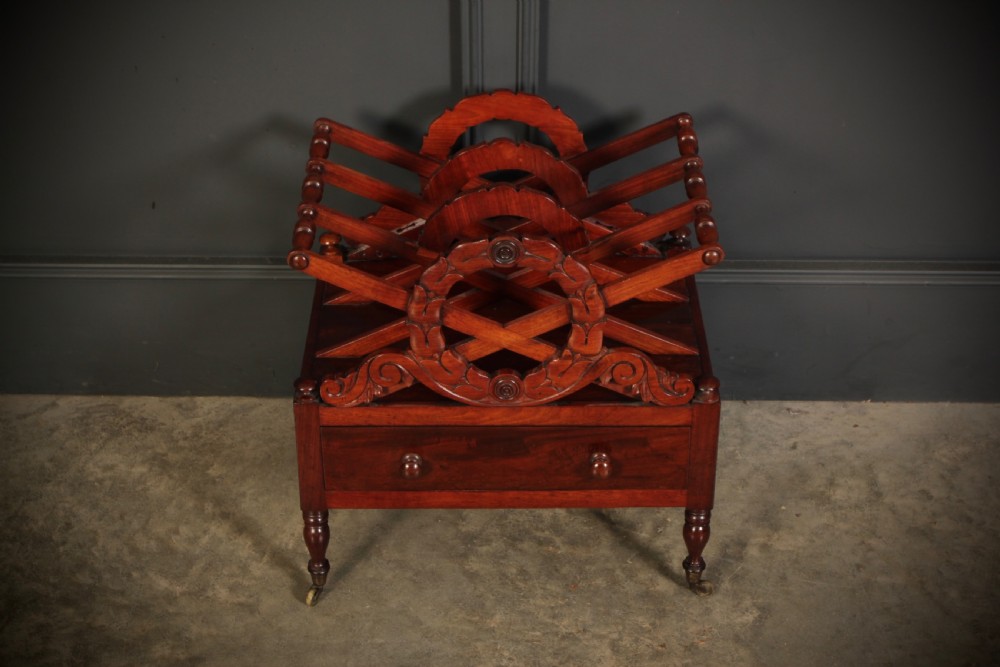 A William IV dark rosewood Canterbury magazine rack featuring four open compartments with carved decorative divisions above a single base drawer on turned legs with brass castors. View V