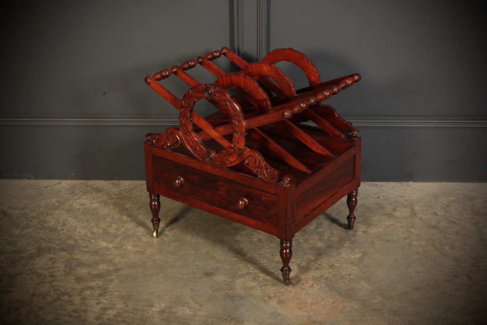 A William IV dark rosewood Canterbury magazine rack featuring four open compartments with carved decorative divisions above a single base drawer on turned legs with brass castors. View VI