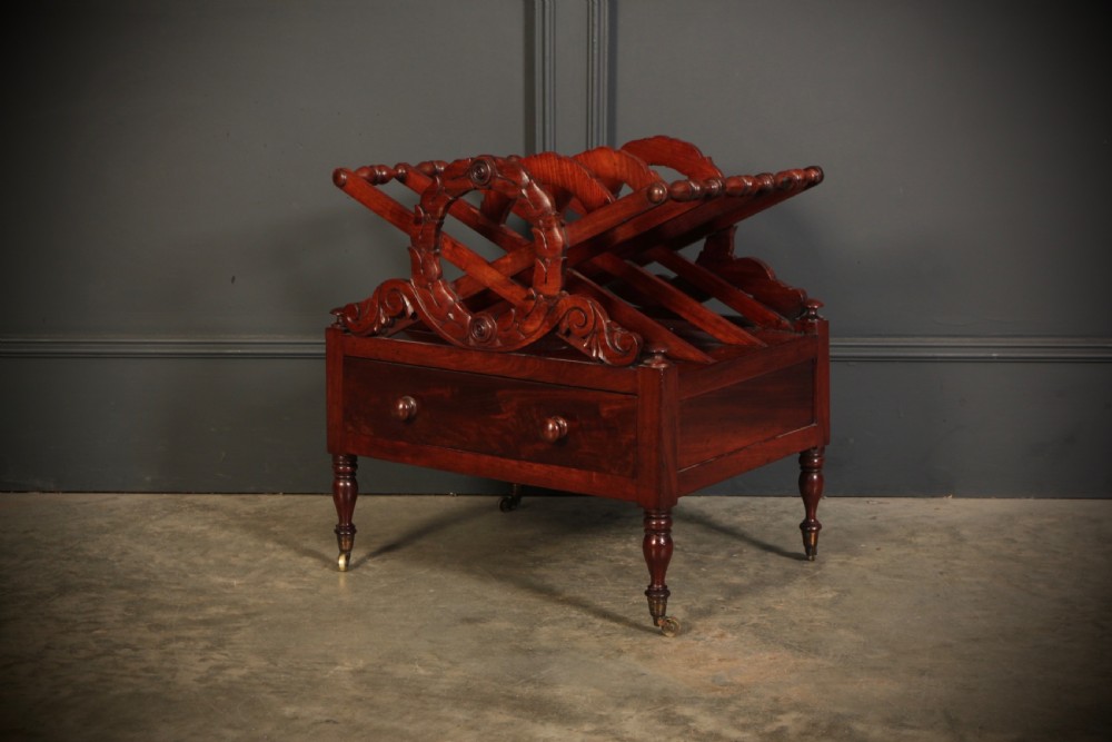 A William IV dark rosewood Canterbury magazine rack featuring four open compartments with carved decorative divisions above a single base drawer on turned legs with brass castors. View VII