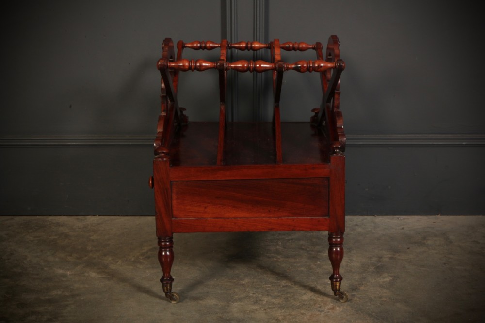 A William IV dark rosewood Canterbury magazine rack featuring four open compartments with carved decorative divisions above a single base drawer on turned legs with brass castors. View IX