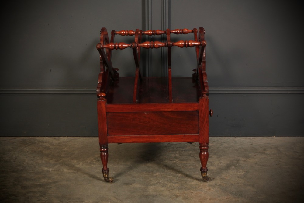 A William IV dark rosewood Canterbury magazine rack featuring four open compartments with carved decorative divisions above a single base drawer on turned legs with brass castors. View X