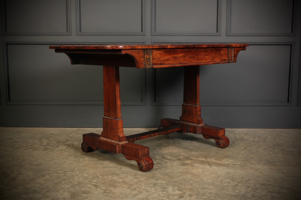 A Regency rosewood library writing table with rounded corners, carved trestle supports, a low stretcher, and scrolled feet. View V