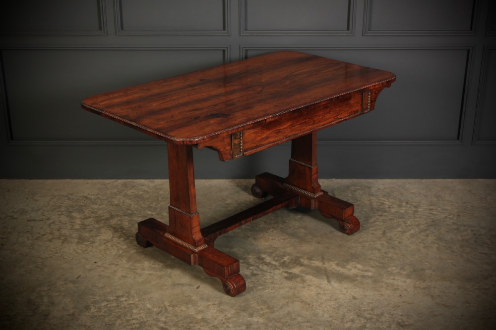 A Regency rosewood library writing table with rounded corners, carved trestle supports, a low stretcher, and scrolled feet. View II