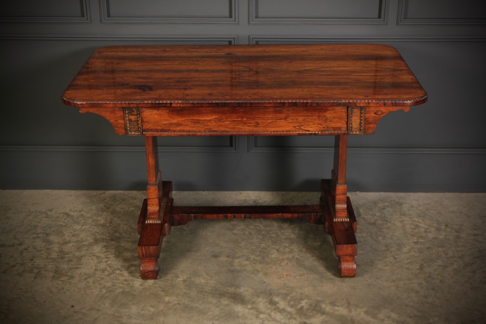 A Regency rosewood library writing table with rounded corners, carved trestle supports, a low stretcher, and scrolled feet.
