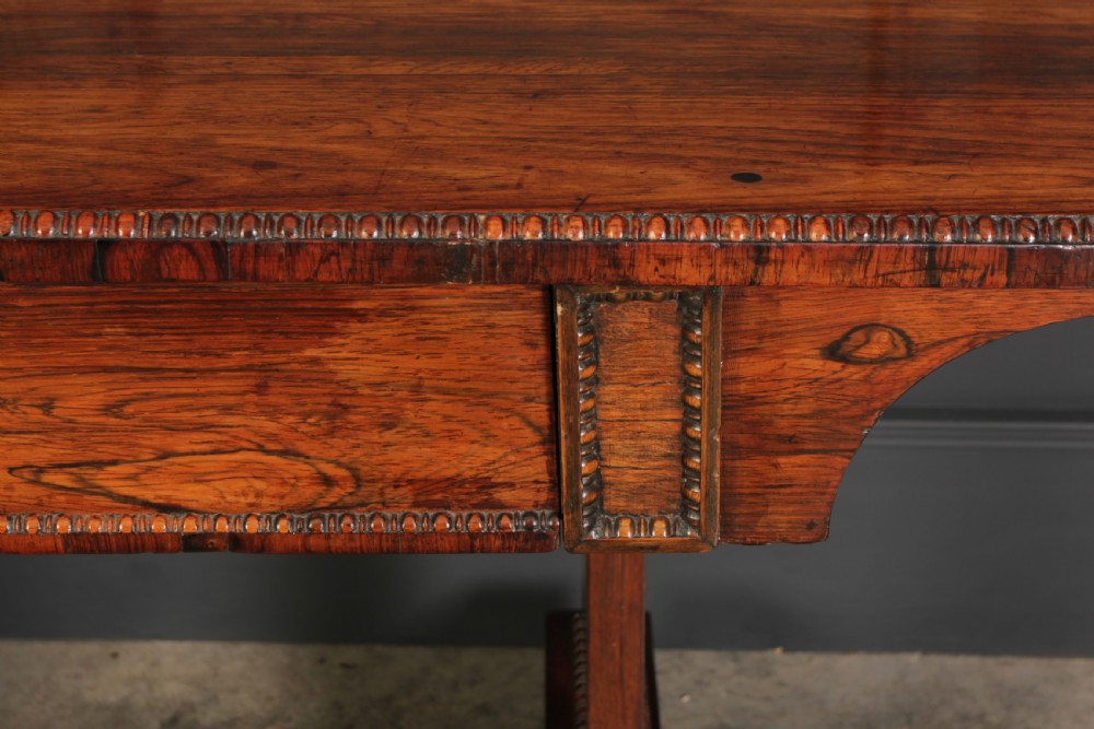 A Regency rosewood library writing table with rounded corners, carved trestle supports, a low stretcher, and scrolled feet. View VI
