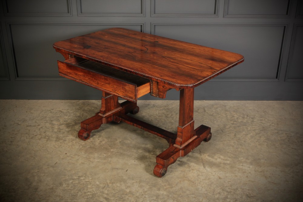A Regency rosewood library writing table with rounded corners, carved trestle supports, a low stretcher, and scrolled feet. View VII