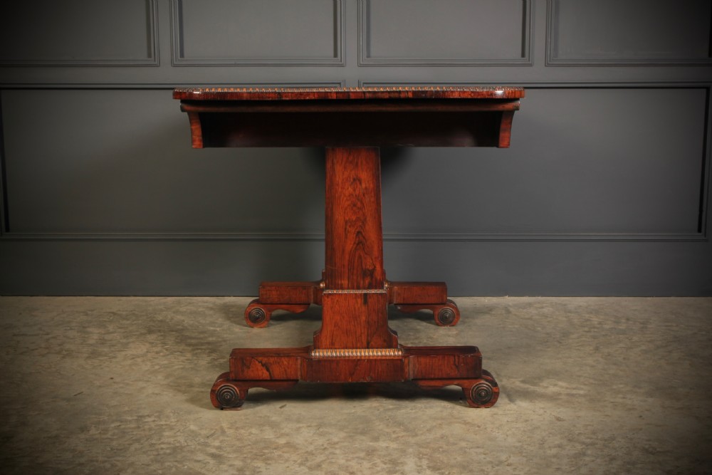 A Regency rosewood library writing table with rounded corners, carved trestle supports, a low stretcher, and scrolled feet. View VIII