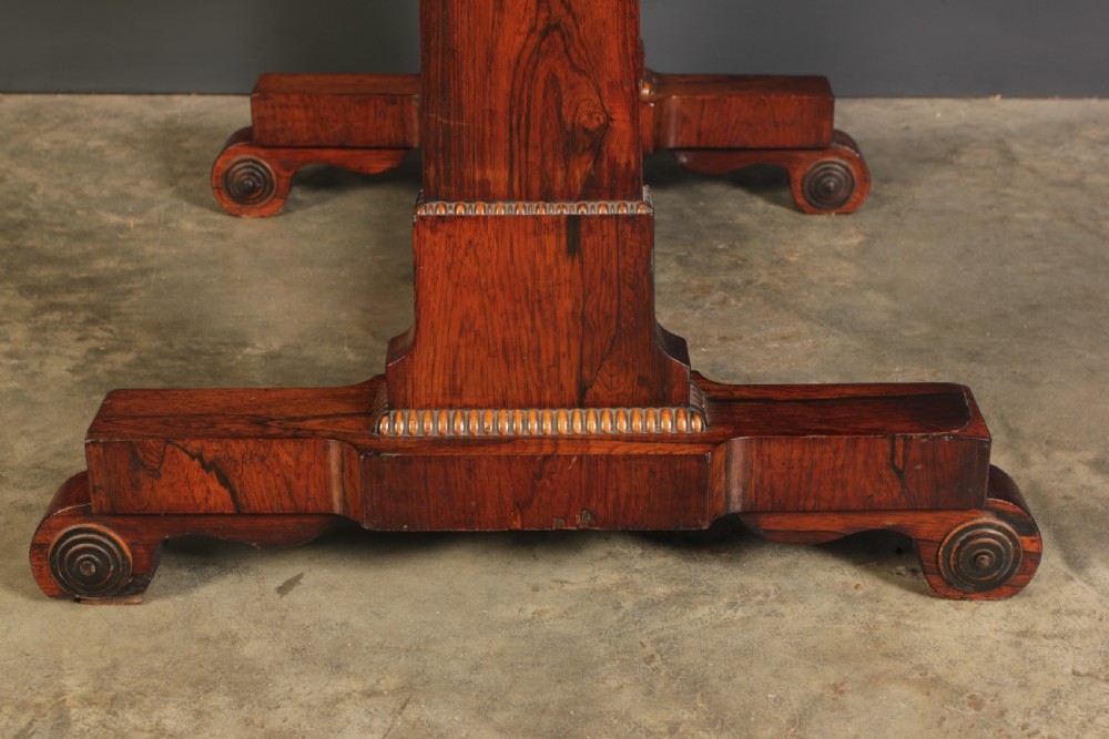 A Regency rosewood library writing table with rounded corners, carved trestle supports, a low stretcher, and scrolled feet. View IX