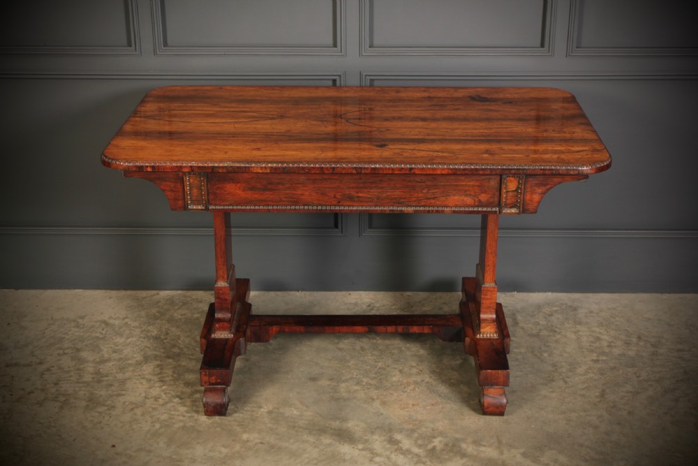 A Regency rosewood library writing table with rounded corners, carved trestle supports, a low stretcher, and scrolled feet. View X