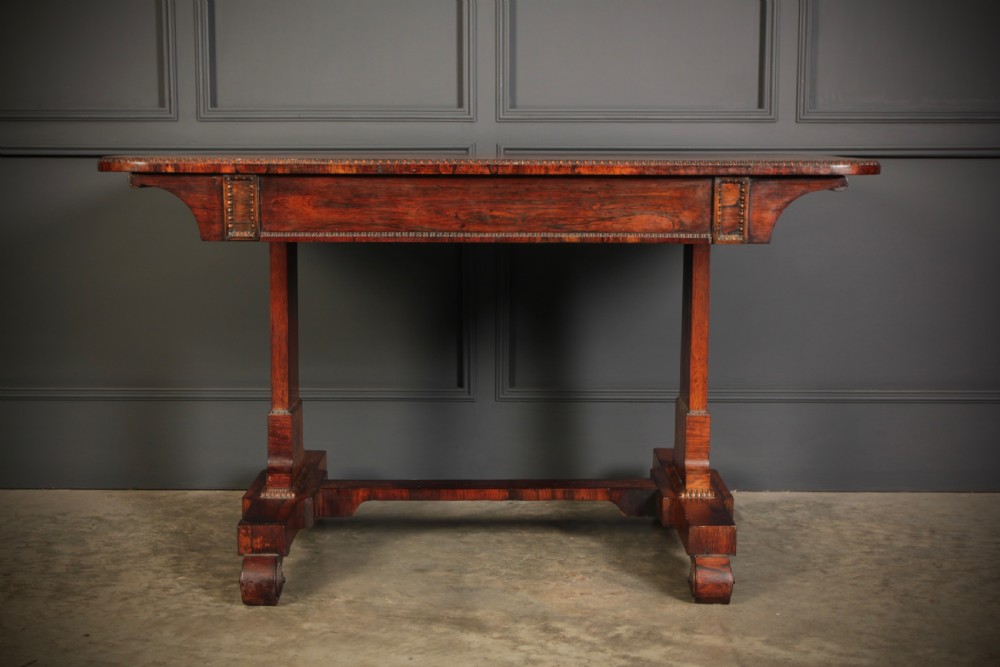 A Regency rosewood library writing table with rounded corners, carved trestle supports, a low stretcher, and scrolled feet. View XI