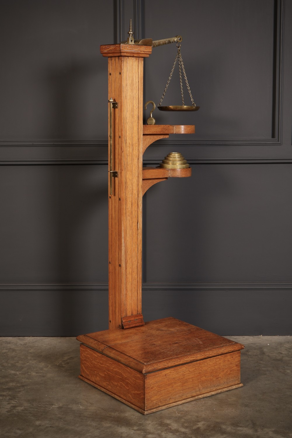 Victorian floor-standing personal weighing scales crafted from oak with brass fittings, balance arm, pan, stacked weights, and a wooden base platform.