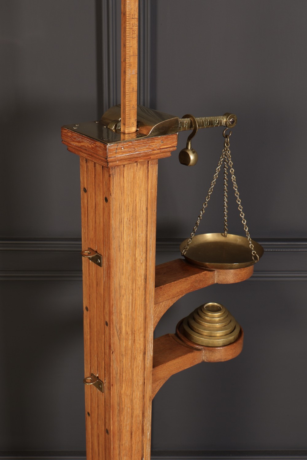 Victorian floor-standing personal weighing scales crafted from oak with brass fittings, balance arm, pan, stacked weights, and a wooden base platform. View VI