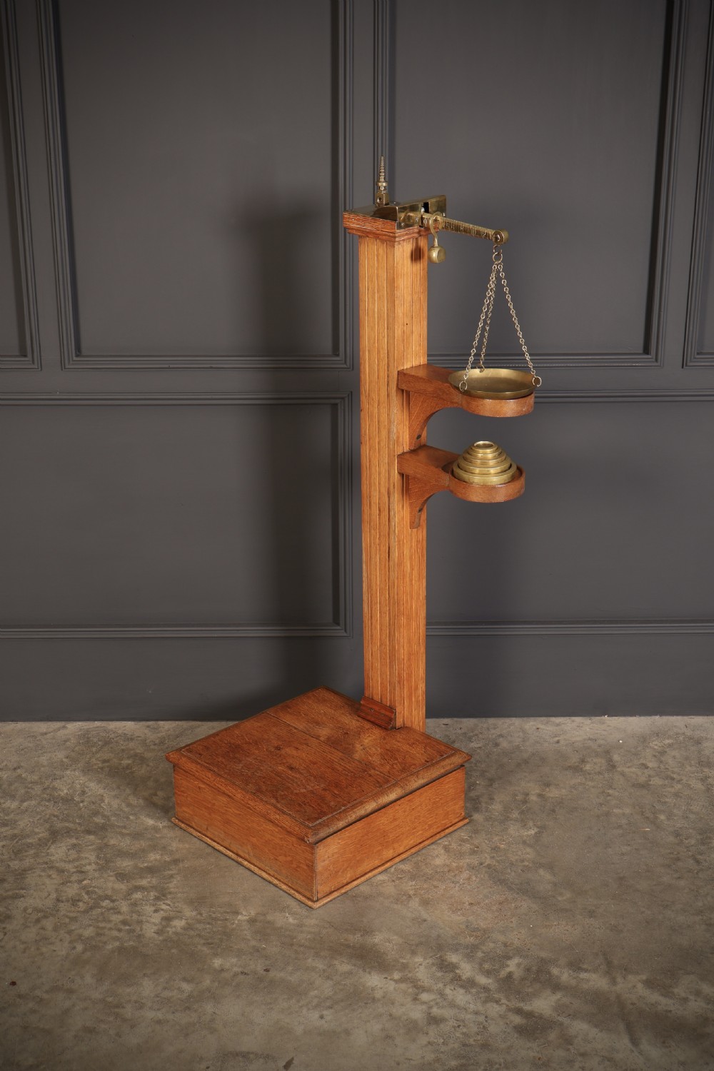 Victorian floor-standing personal weighing scales crafted from oak with brass fittings, balance arm, pan, stacked weights, and a wooden base platform. View IX