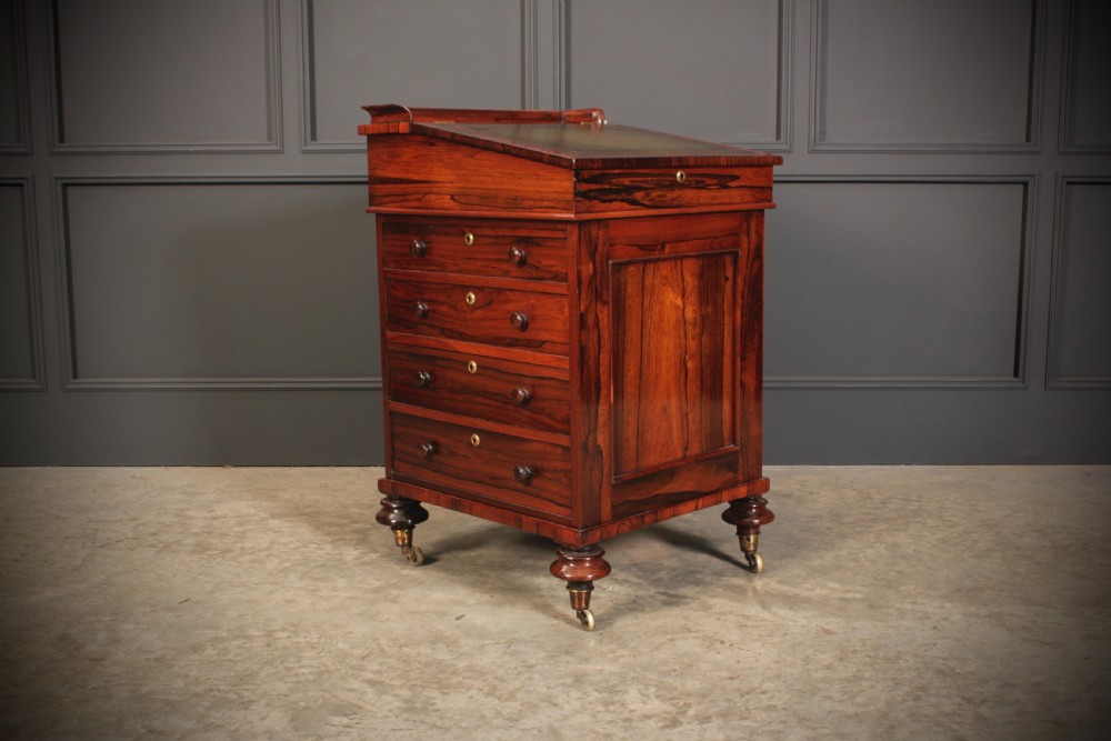 A William IV rosewood Davenport desk featuring a green leather sloped writing surface, side drawers with wooden knob handles, and turned feet on brass castors. View VII