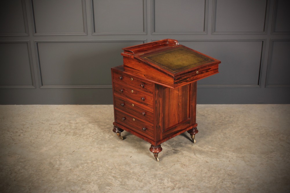 A William IV rosewood Davenport desk featuring a green leather sloped writing surface, side drawers with wooden knob handles, and turned feet on brass castors. View II