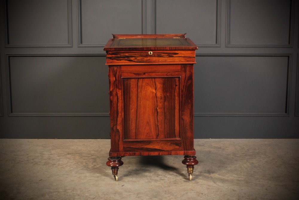A William IV rosewood Davenport desk featuring a green leather sloped writing surface, side drawers with wooden knob handles, and turned feet on brass castors. View III