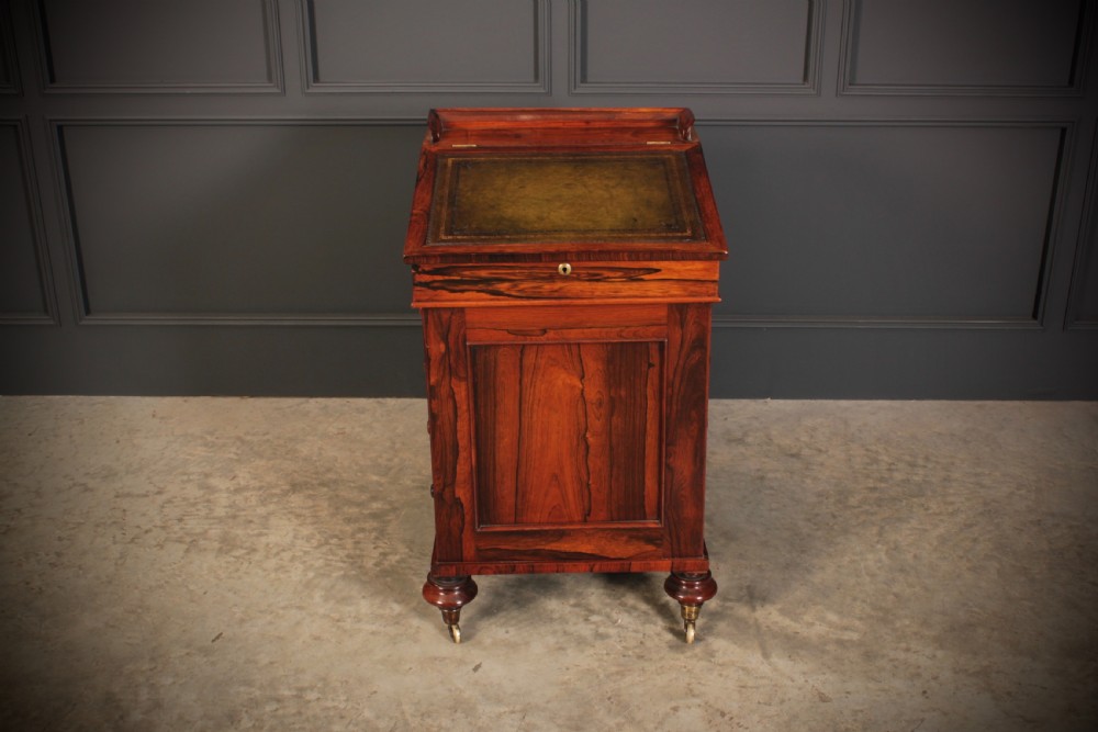 A William IV rosewood Davenport desk featuring a green leather sloped writing surface, side drawers with wooden knob handles, and turned feet on brass castors. View IV