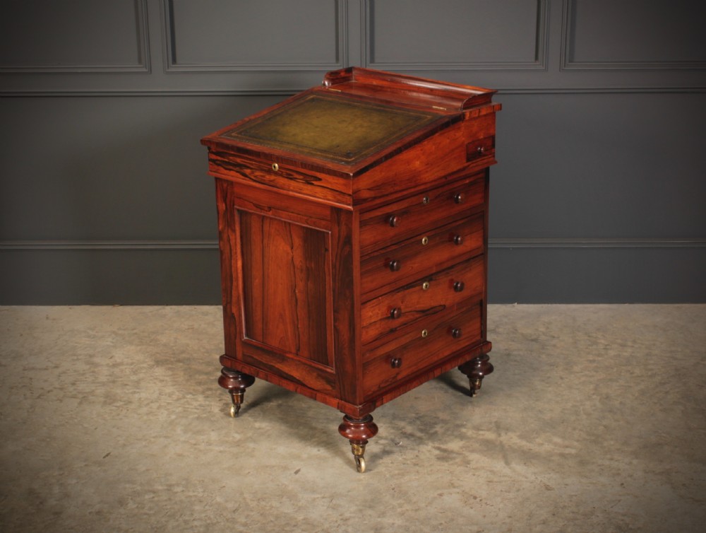 A William IV rosewood Davenport desk featuring a green leather sloped writing surface, side drawers with wooden knob handles, and turned feet on brass castors.