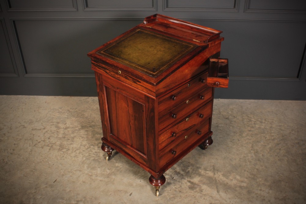 A William IV rosewood Davenport desk featuring a green leather sloped writing surface, side drawers with wooden knob handles, and turned feet on brass castors. View X