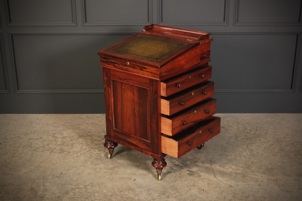 A William IV rosewood Davenport desk featuring a green leather sloped writing surface, side drawers with wooden knob handles, and turned feet on brass castors. View XI
