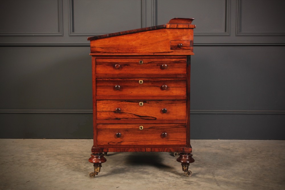 A William IV rosewood Davenport desk featuring a green leather sloped writing surface, side drawers with wooden knob handles, and turned feet on brass castors. View XIII