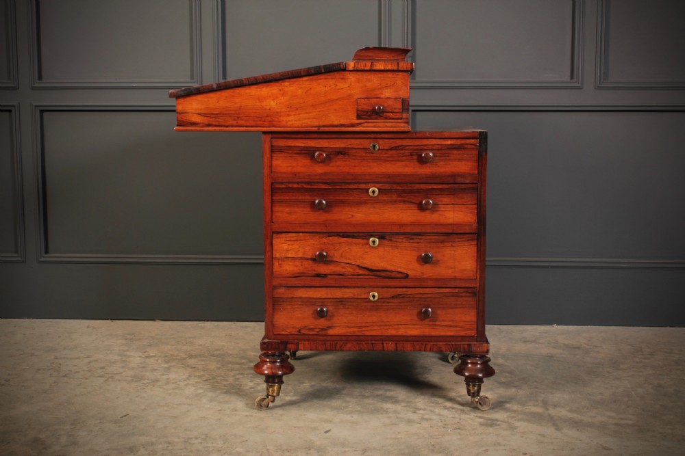 A William IV rosewood Davenport desk featuring a green leather sloped writing surface, side drawers with wooden knob handles, and turned feet on brass castors. View XV
