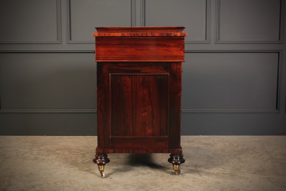 A William IV rosewood Davenport desk featuring a green leather sloped writing surface, side drawers with wooden knob handles, and turned feet on brass castors. View XVI